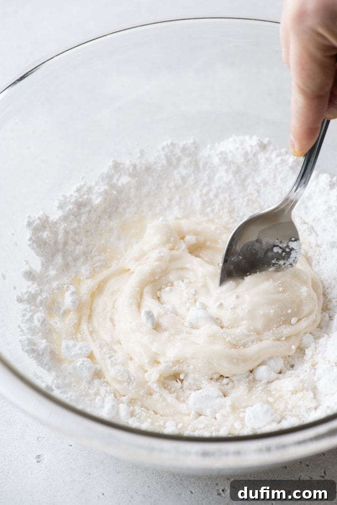 Royal icing ingredients being mixed together with a spoon in a clear glass bowl.