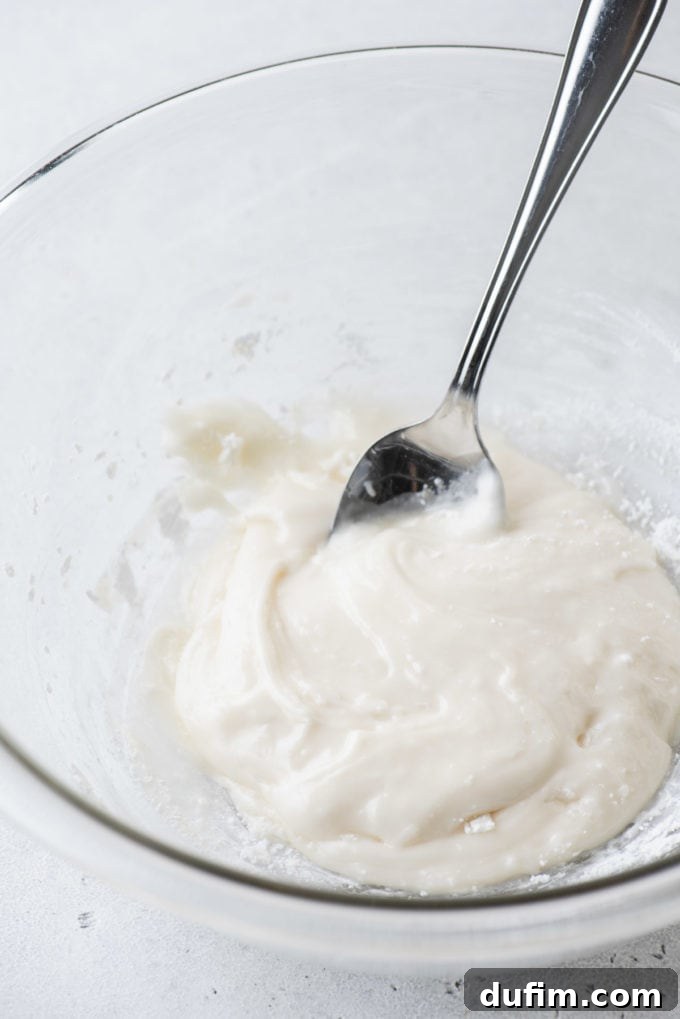 Royal icing in a clear glass bowl with a spoon.