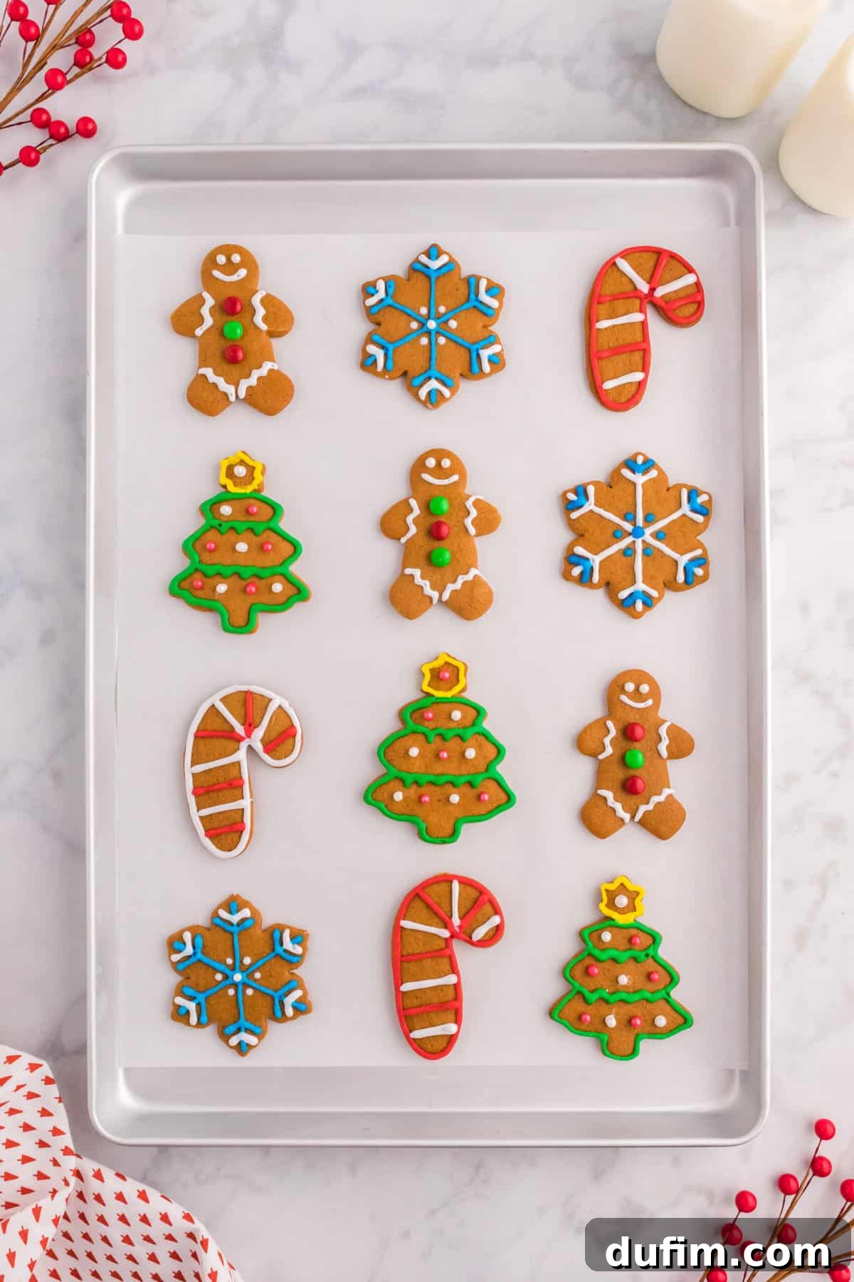 An assortment of gingerbread cookies decorated with royal icing, lined in rows on a cookie sheet lined with parchment paper.