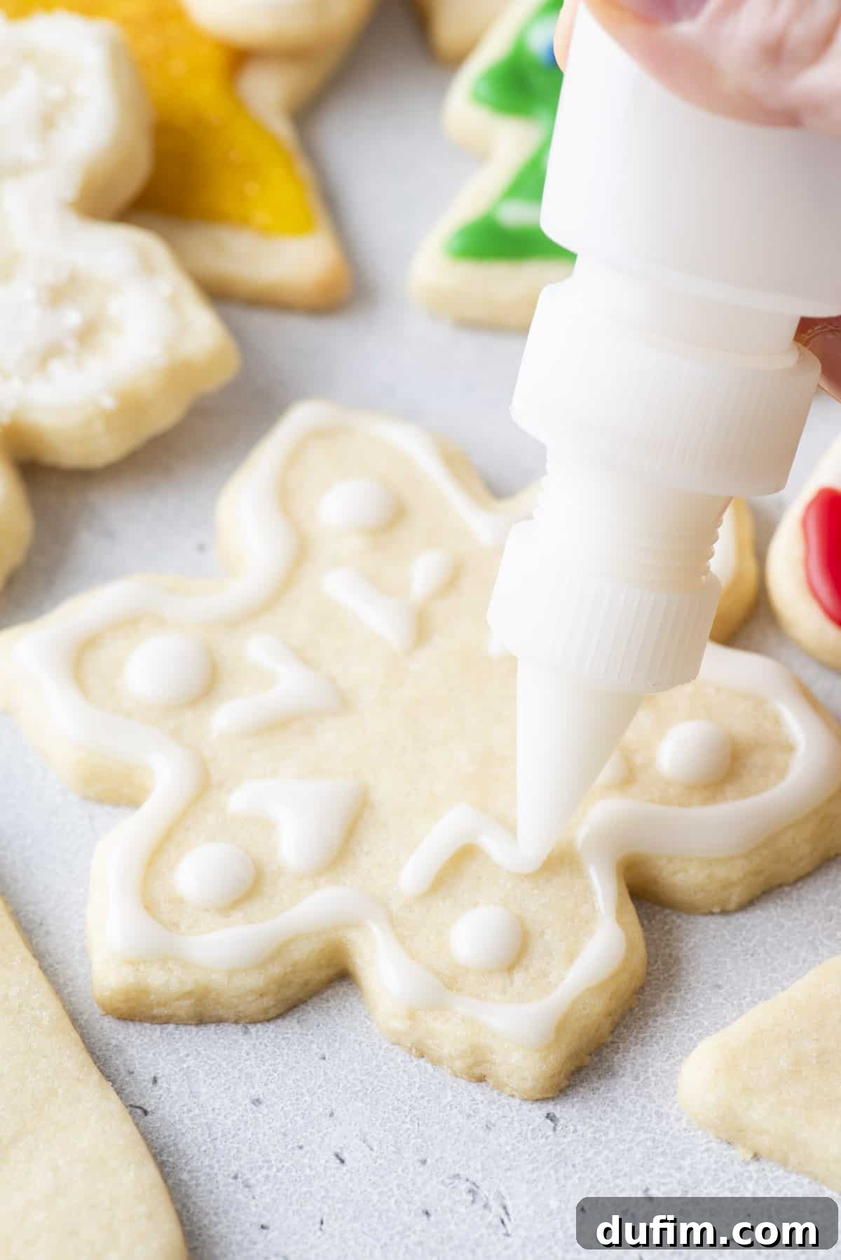 White royal icing being piped onto a snowflake-shaped cookie with a squeeze bottle.
