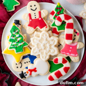 A collection of sugar cookies decorated with royal icing in a Christmas theme on a white plate.