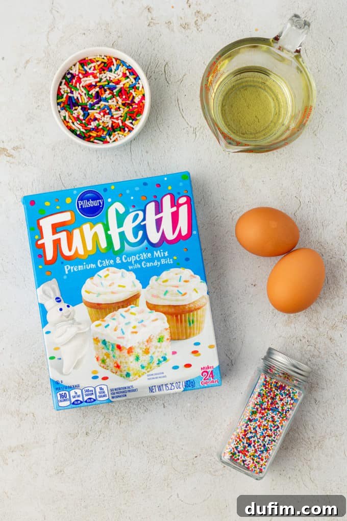 Ingredients for cheerful Funfetti cake mix cookies: a box of Funfetti cake mix, two large fresh eggs, a vibrant bowl of sprinkles, and golden vegetable oil, all ready to be combined.