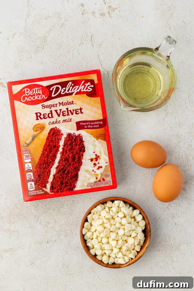 Ingredients for classic red velvet cake mix cookies: a box of red velvet cake mix, two fresh eggs, a wooden bowl filled with white chocolate chips, and vegetable oil, awaiting combination.