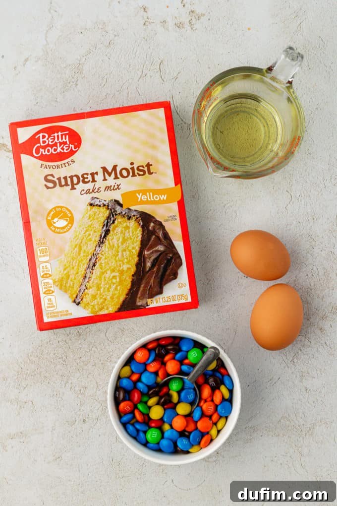 Key ingredients for delightful M&M cookies: a bottle of vegetable oil, two large fresh eggs, and a small white bowl brimming with colorful M&M's candies, ready to be incorporated.
