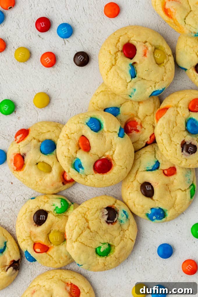 Freshly baked M&M cake mix cookies scattered around, with extra M&M's sprinkled on top and around them, highlighting their vibrant colors and appealing texture.