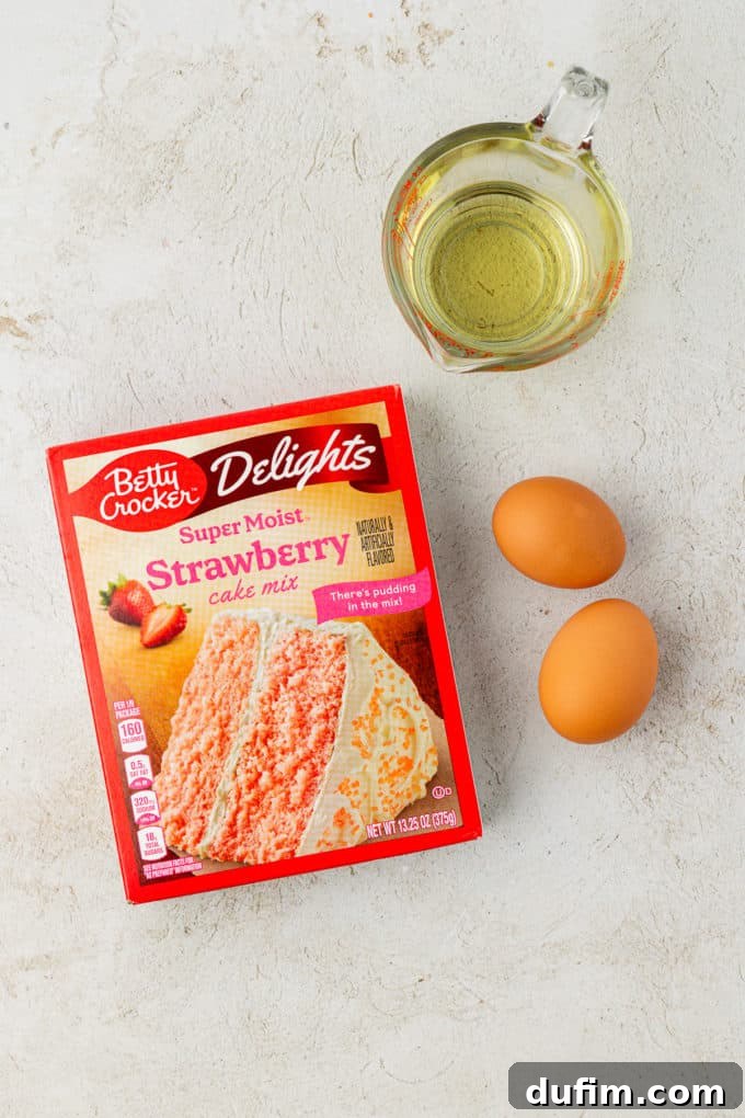 Ingredients for delightful strawberry cake mix cookies: a box of strawberry cake mix, two fresh eggs, and vegetable oil, neatly arranged and ready for combining.