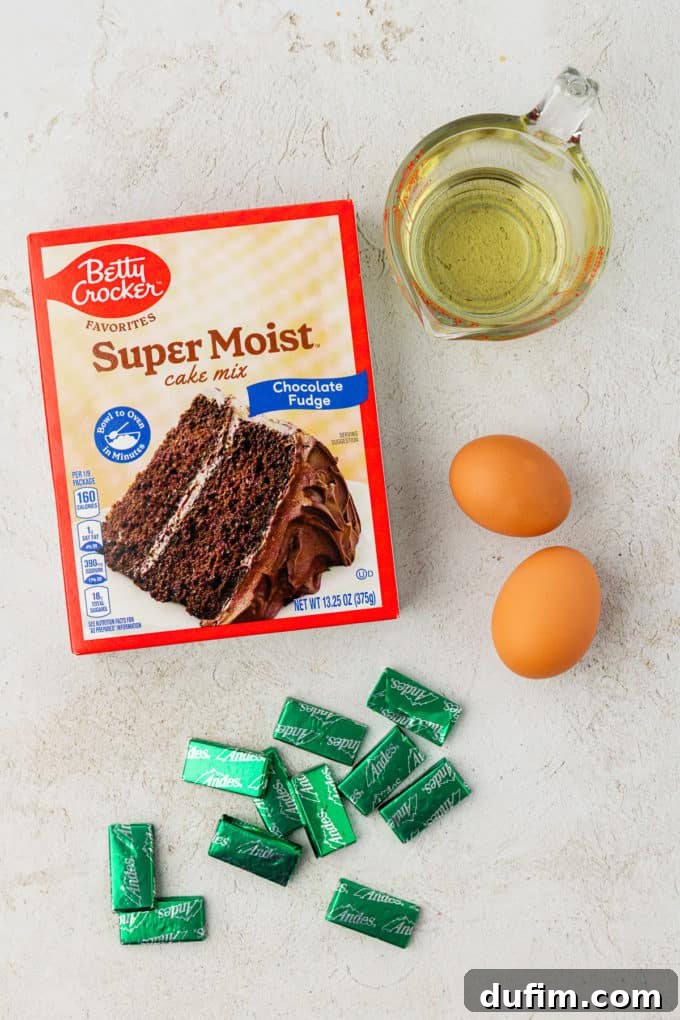 Ingredients for refreshing Andes mint cake mix cookies: a box of chocolate cake mix, a pile of Andes mint candies, two fresh eggs, and vegetable oil, ready for combining and baking.
