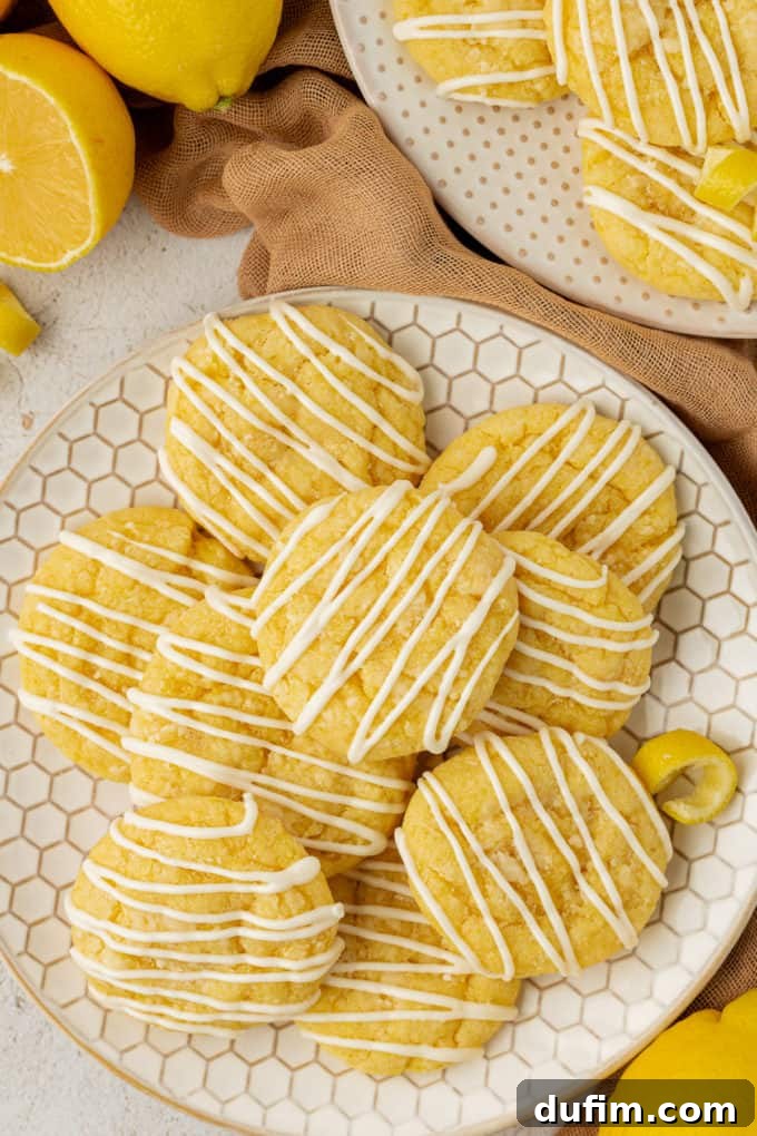 Zesty lemon cake mix cookies elegantly arranged on a honeycomb-patterned plate, surrounded by tan cloth and fresh lemons. Another plate of cookies is visible in the background, completing a refreshing dessert scene.
