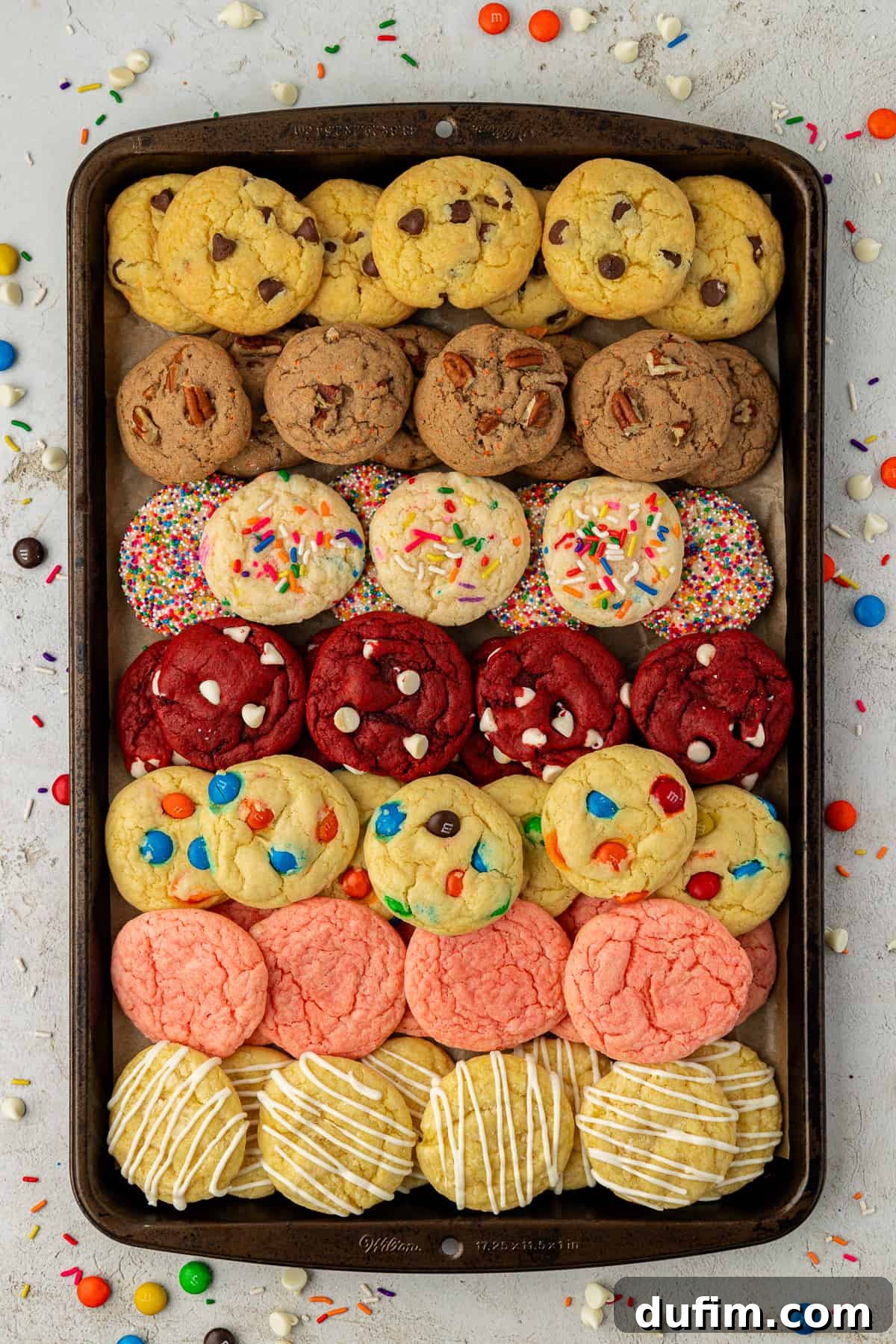 A delectable spread of assorted cake mix cookies, showcasing a variety of vibrant flavors and textures. The cookies are arranged enticingly on a baking sheet, surrounded by loose M&M's, Reese's Pieces, and colorful sprinkles, ready to be enjoyed.