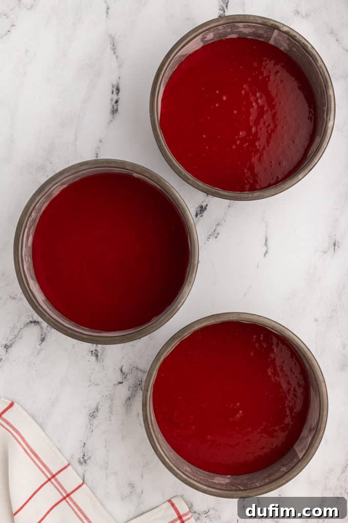 Homemade Red Velvet Cake Perfection 13 Three cake pans filled uniformly with vibrant red velvet cake batter, ready for baking to achieve perfectly even layers.