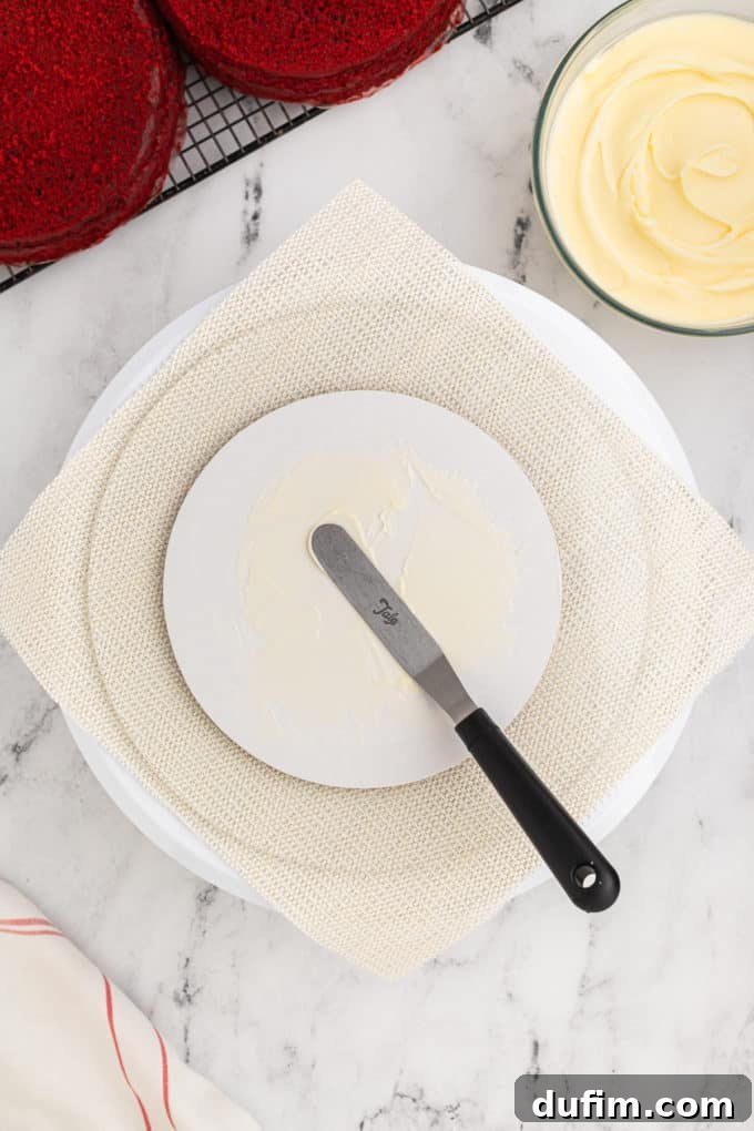 Homemade Red Velvet Cake Perfection 15 A pristine white cake stand is prepped for cake assembly, with a bowl of creamy cream cheese frosting and a wire rack holding cooled red velvet cake layers positioned nearby, ready for decorating.
