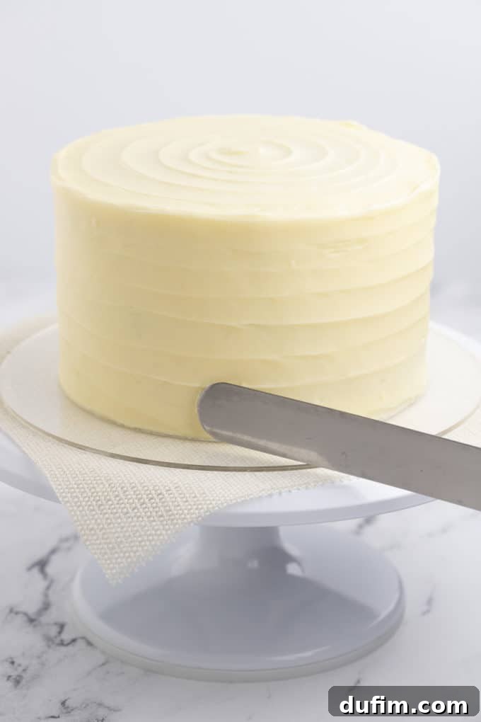Homemade Red Velvet Cake Perfection 20 A red velvet cake on a white cake stand is being meticulously frosted with smooth cream cheese frosting, creating a pristine white canvas for decoration.