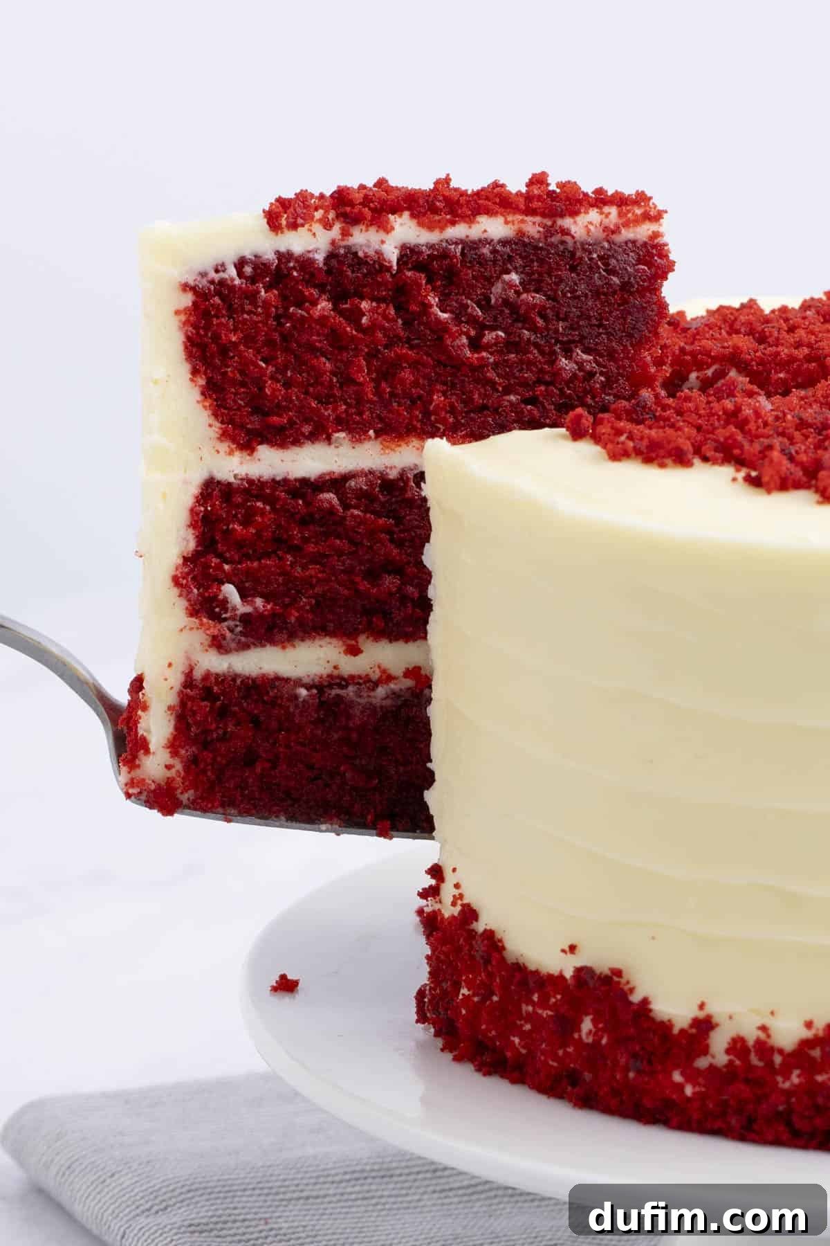 Homemade Red Velvet Cake Perfection 4 A slice of vibrant red velvet cake being carefully lifted from the main cake with a serving knife, showcasing its distinct layers and creamy frosting.