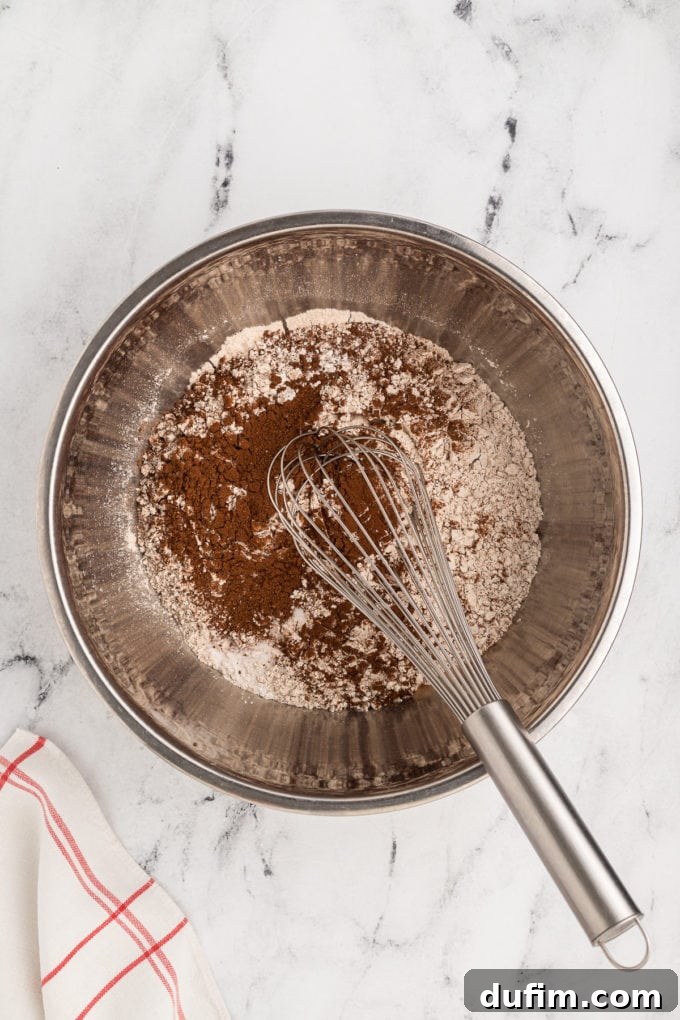 Homemade Red Velvet Cake Perfection 7 Dry ingredients for red velvet cake, including flour, cocoa powder, sugar, and leavening agents, being expertly mixed in a silver bowl with a wire whisk, ensuring an even distribution for the perfect cake.