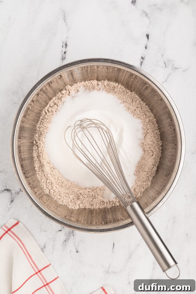 Homemade Red Velvet Cake Perfection 8 A close-up view of the combined dry ingredients for red velvet cake, featuring flour, cocoa, and sugar, being meticulously blended with a wire whisk in a silver bowl to prepare for wet ingredients.