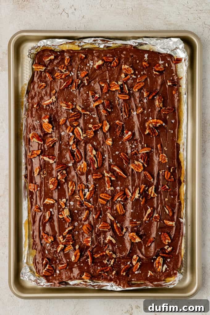 A sheet pan filled with Christmas Crack candy, half generously covered with chopped pecans and a sprinkle of sea salt.