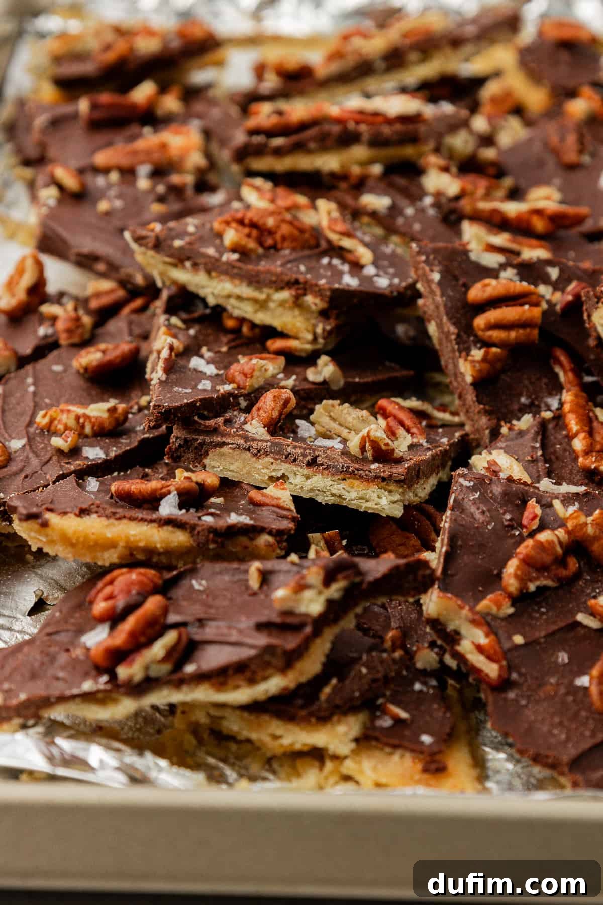 Delicious Christmas Crack candy with pecans and sea salt, arranged on a sheet pan lined with aluminum foil, ready to be enjoyed.