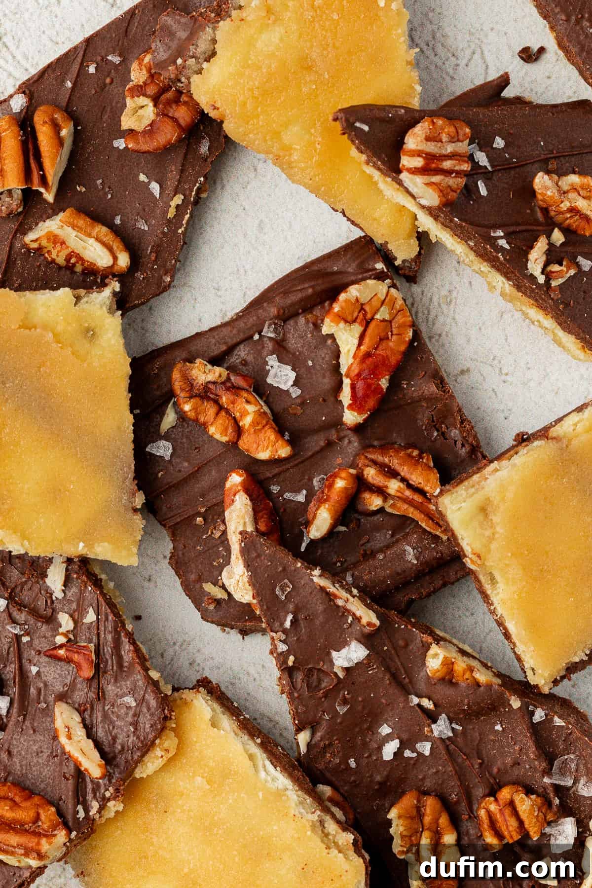 Close-up of numerous Christmas Crack candy pieces, topped with pecans and sea salt, arranged artistically for display.