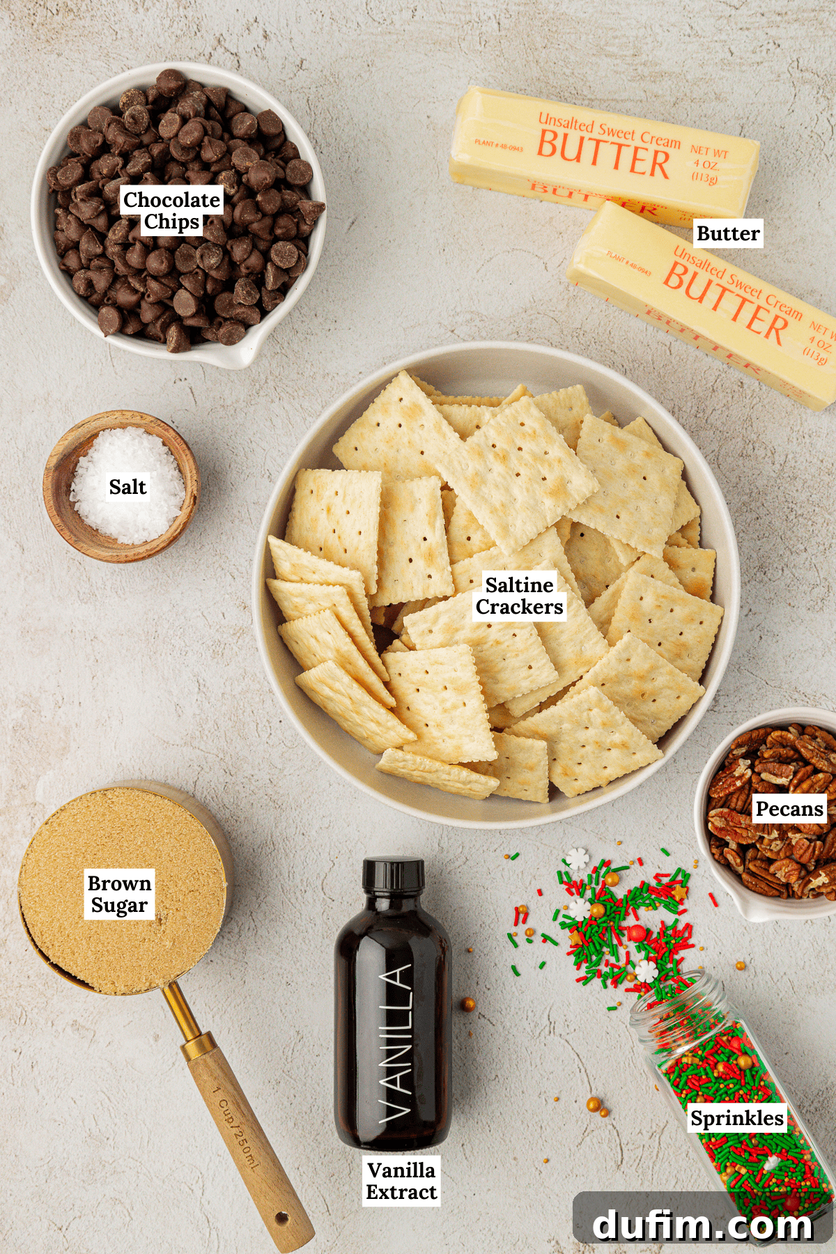 Overhead view of Christmas Crack ingredients: saltine crackers, brown sugar, semi-sweet chocolate chips, sea salt, sprinkles, butter sticks, and pecans, neatly arranged for baking.