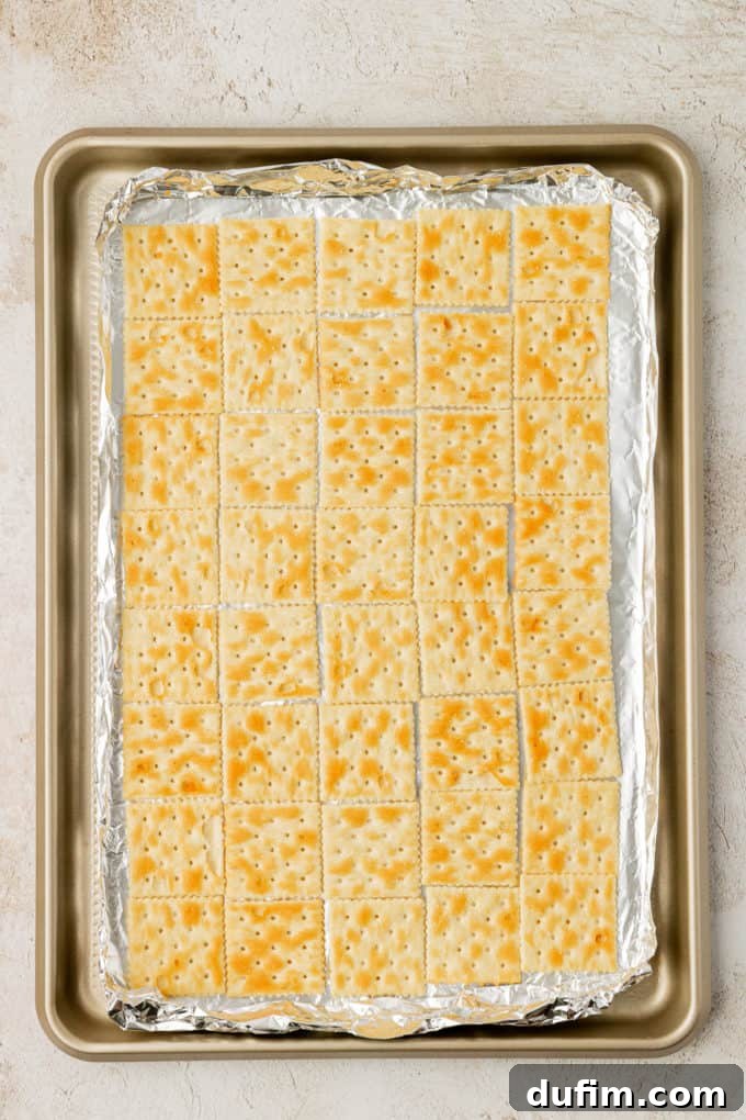 A baking sheet lined with aluminum foil, covered completely with a single, neatly arranged layer of saltine crackers.