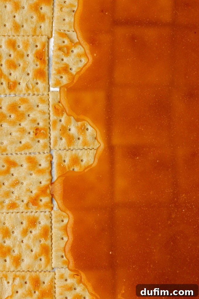 Hot, bubbling brown sugar and butter toffee being poured and partially spread over the single layer of saltine crackers on a baking sheet.