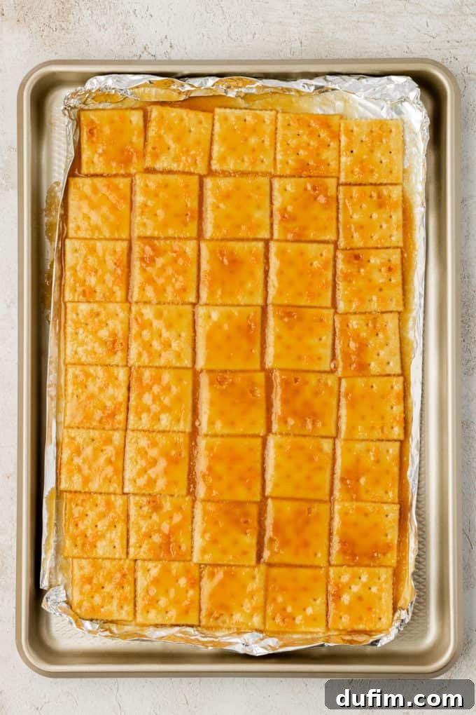 A full sheet pan of baked saltine crackers coated with golden-brown toffee, fresh out of the oven and still bubbling.