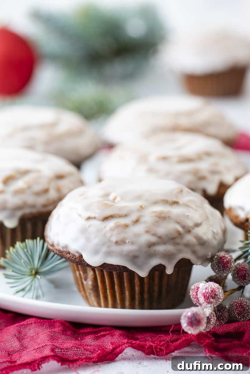 A festive spread of gingerbread muffins with vanilla glaze, beautifully arranged on a white plate with red sugared berries and evergreen branches, epitomizing holiday warmth.