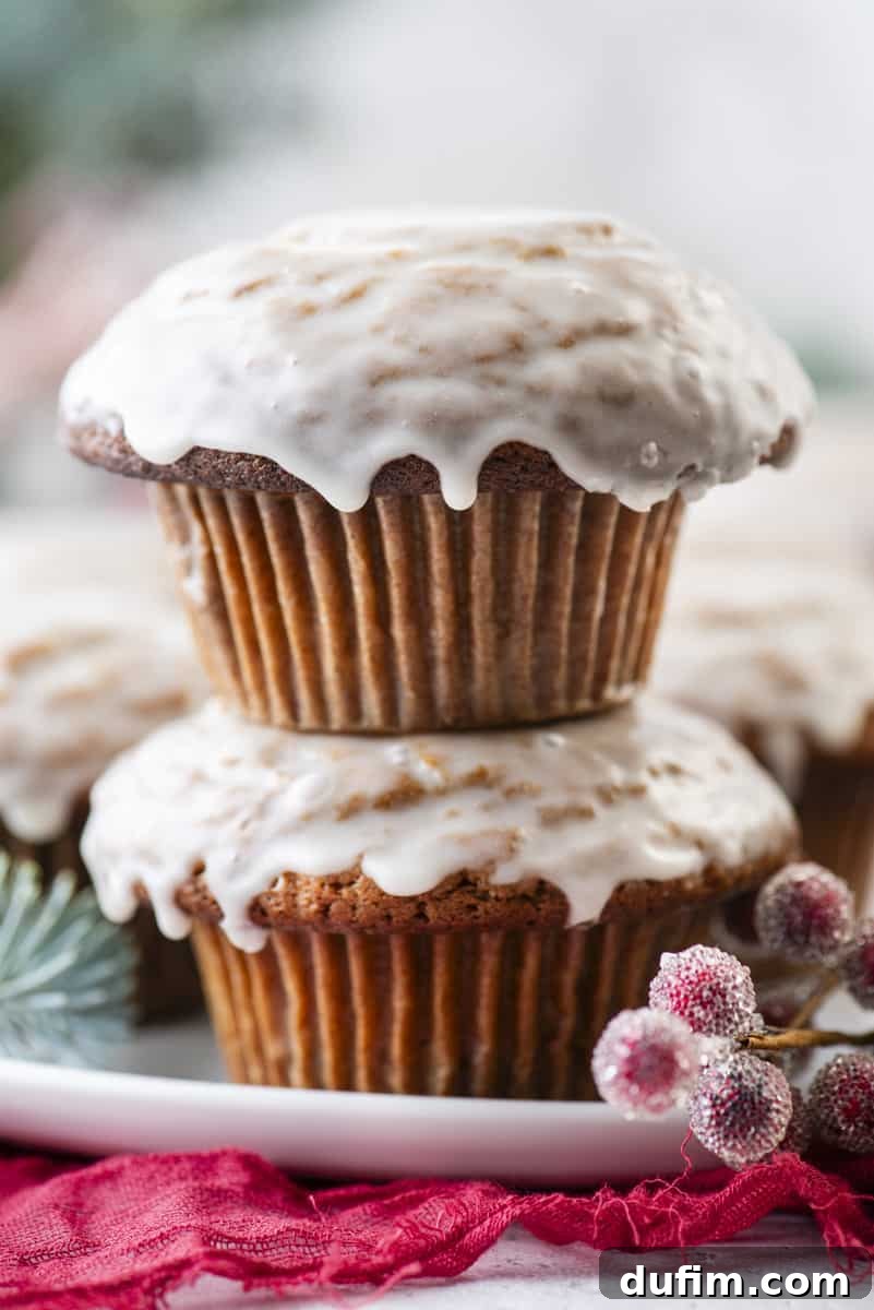 Close-up of gingerbread muffins with a delightful vanilla glaze, elegantly presented on a white plate with vibrant red sugared berries and natural evergreen branches, evoking a warm holiday ambiance.