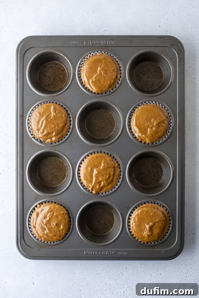 Thick gingerbread muffin dough filling each cup of a muffin pan, perfectly prepped for baking.