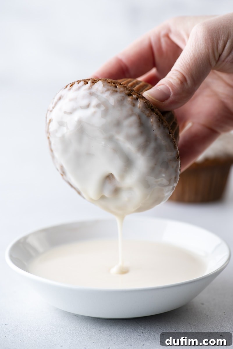 A hand carefully dipping a warm gingerbread muffin into a bowl of luscious vanilla glaze, creating a perfect festive topping.