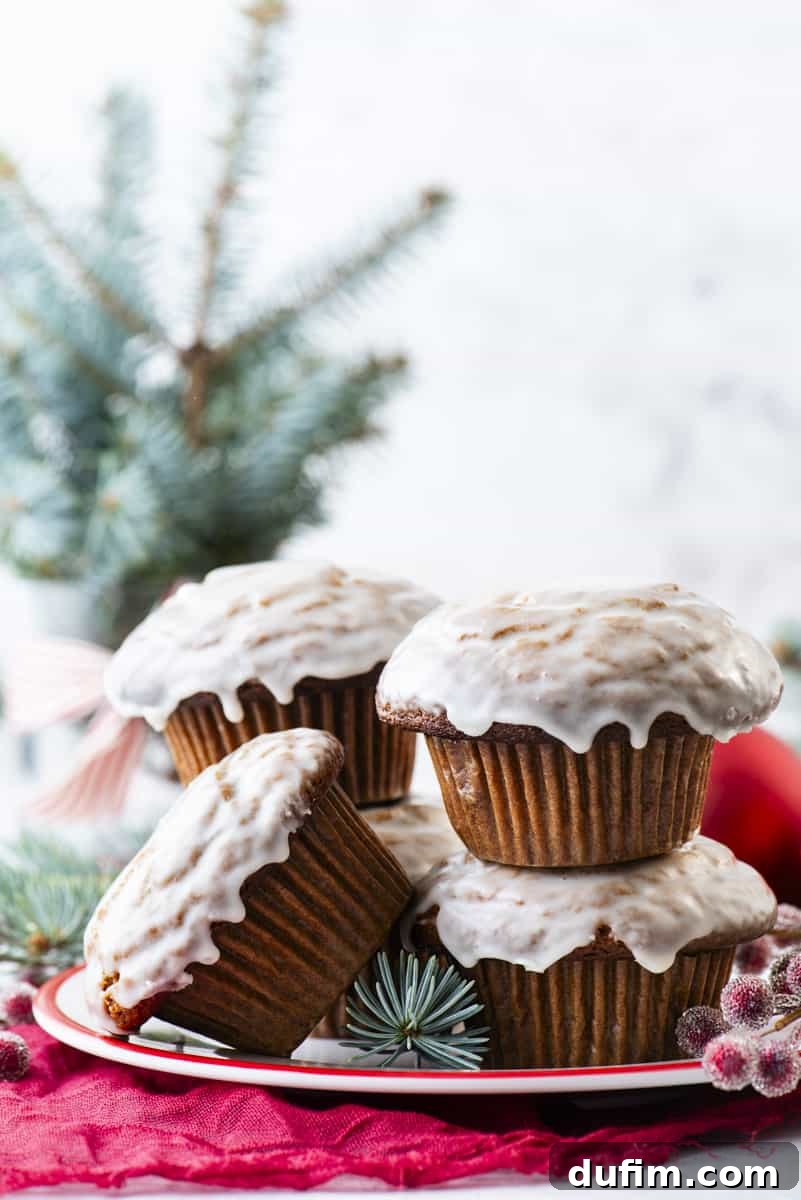 Three gingerbread muffins, artfully arranged with vanilla glaze, on a white plate alongside vibrant red sugared berries and elegant evergreen sprigs, embodying the spirit of winter holidays.