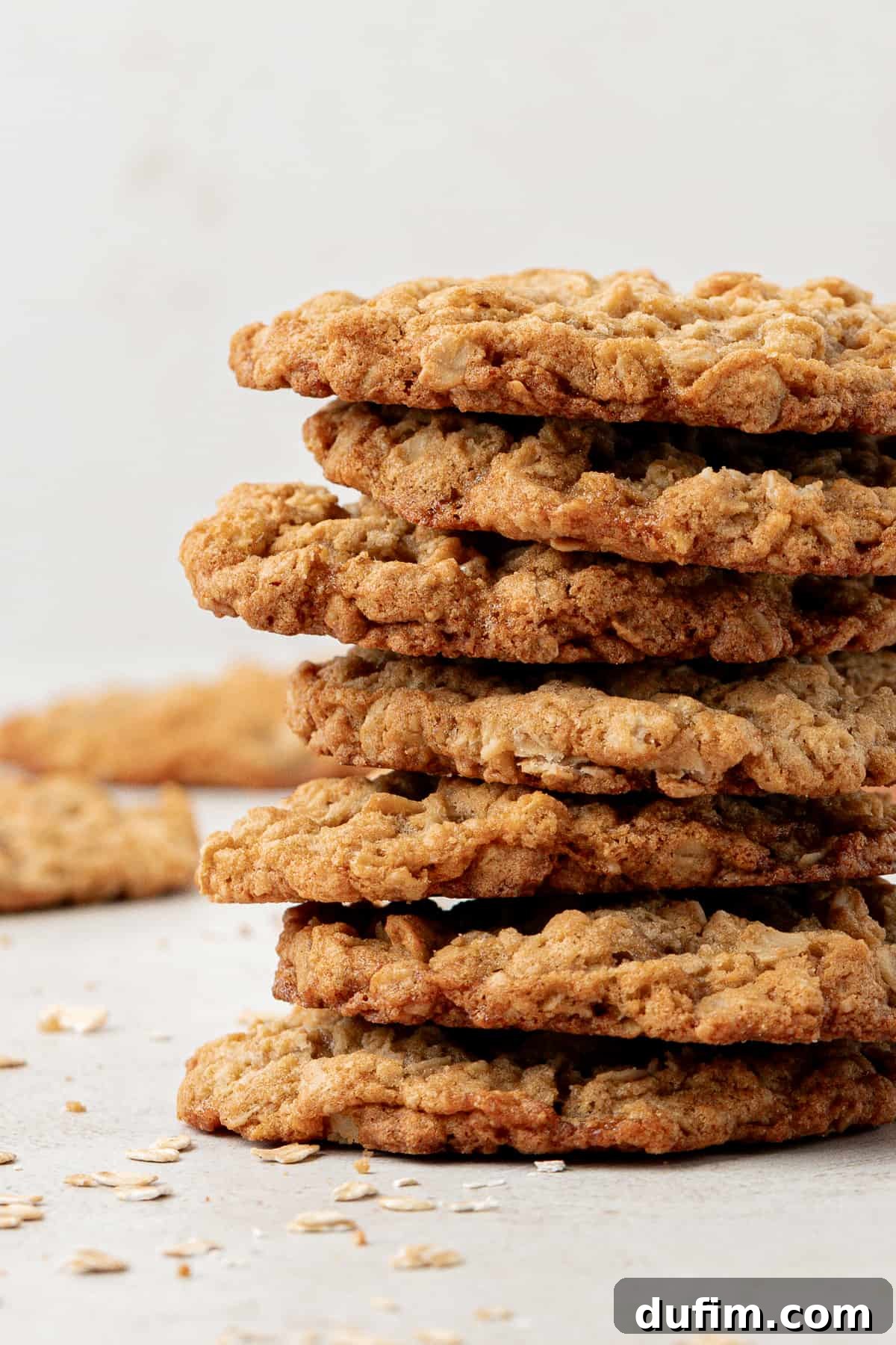 a stack of oatmeal cookies with more cookies and oats sprinkled in the background