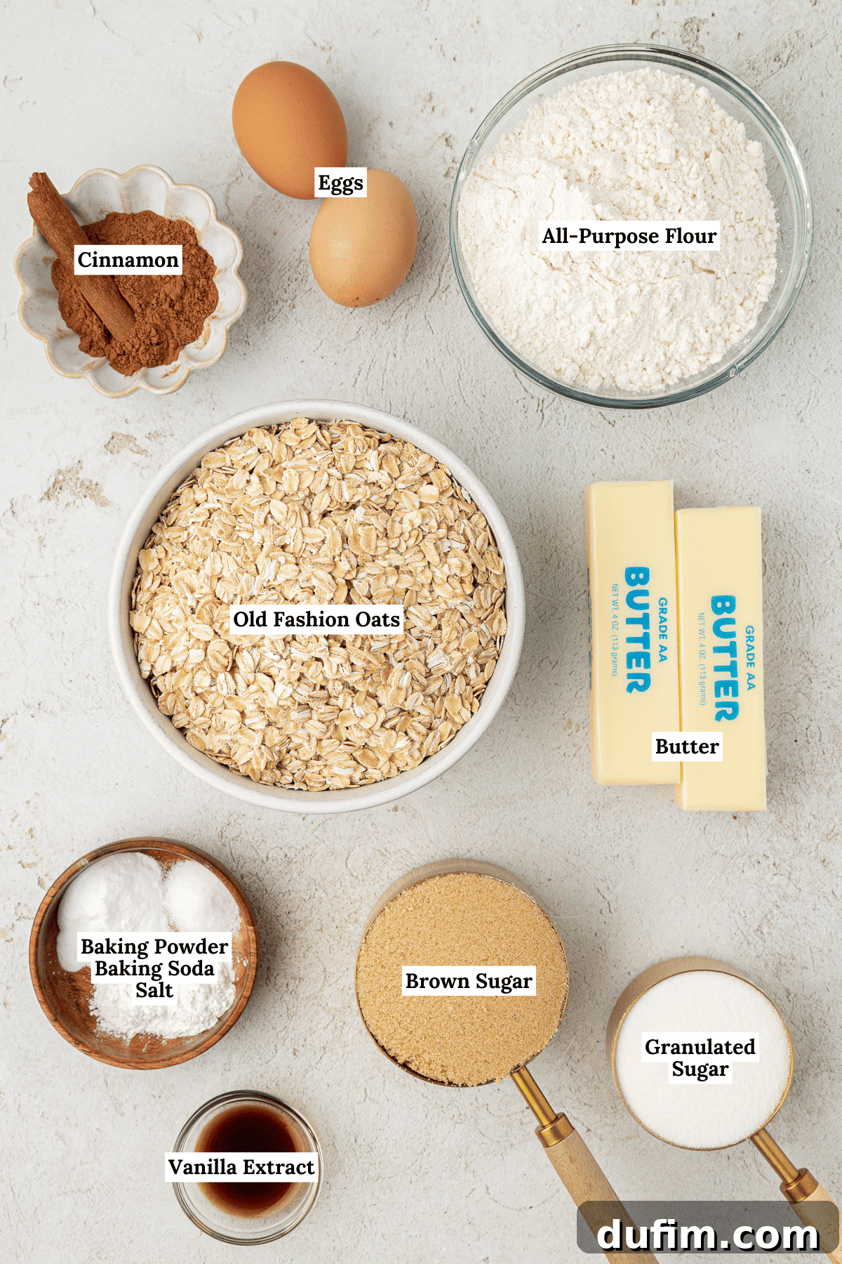 overhead view of oatmeal cookies ingredients including old fashioned oats, two sticks of butter, cinnamon, brown sugar, all-purpose flour, vanilla extract, two eggs, baking powder, baking sugar and salt