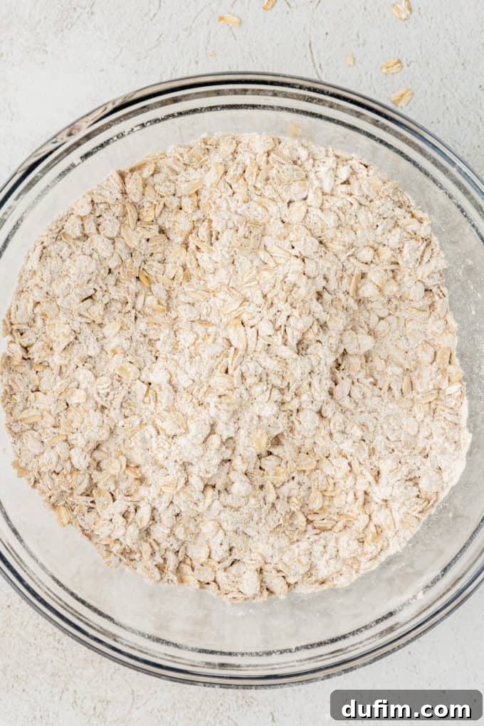 dry ingredients for oatmeal cookies and oats mixed together in a clear glass bowl