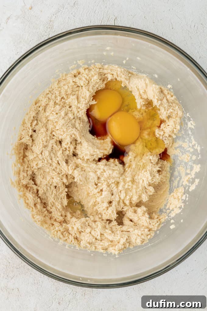 a clear glass bowl with mixed butter, granulated sugar and brown sugar with two eggs and vanilla extract on top