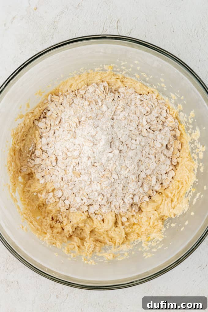 a clear glass bowl with oatmeal cookie mixture with dry oats mix on top of it