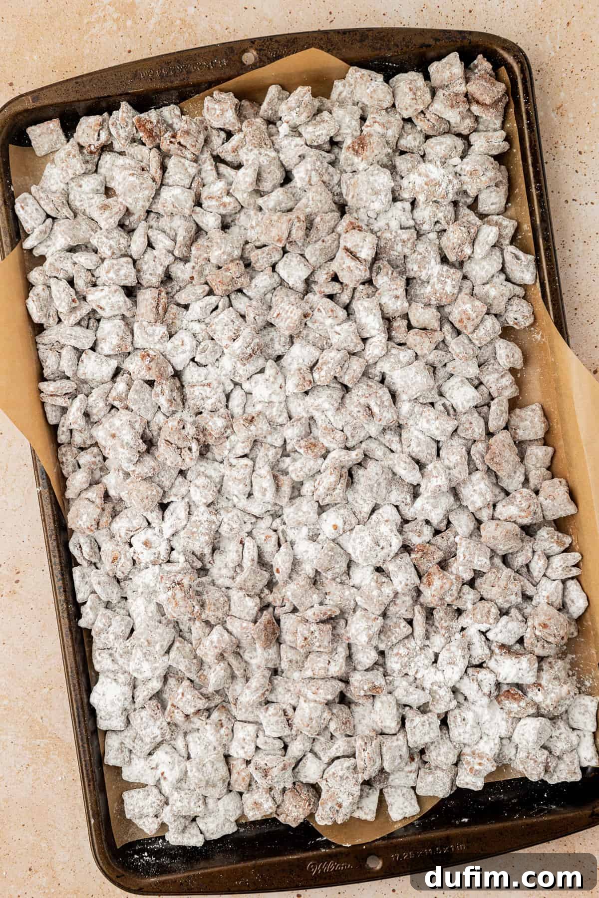 a sheet pan lined with parchment paper full of puppy chow/muddy buddies