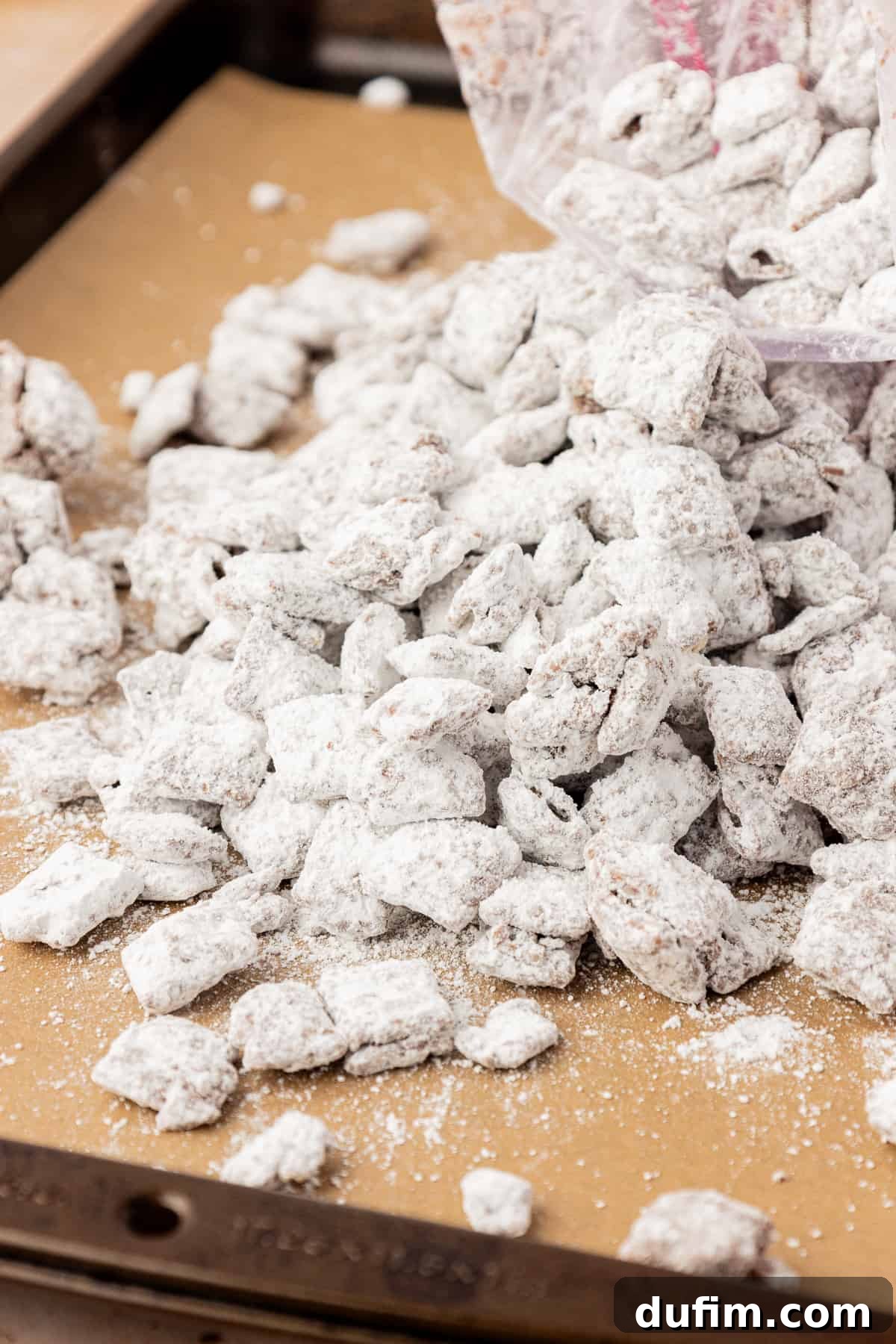 A pile of puppy chow spilled out of a ziploc bag onto a sheet pan lined with parchment paper