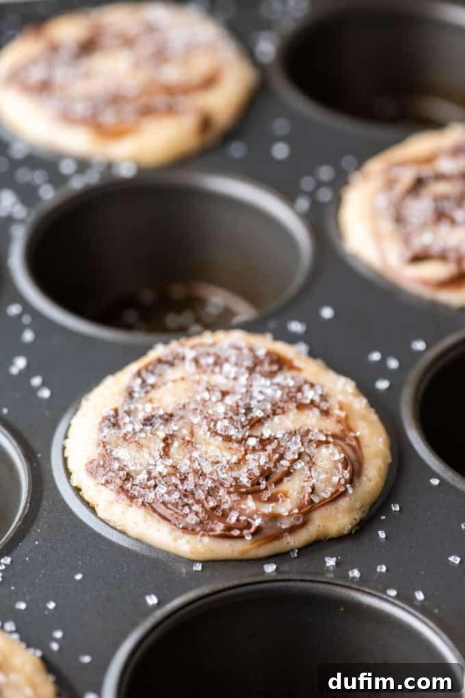A muffin pan with the batter for Nutella swirl muffins filling every other muffin hole, beautifully topped with sparkling sanding sugar.