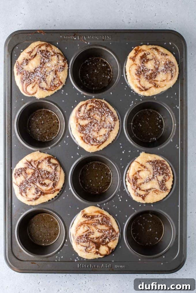 A muffin pan filled with Nutella swirl muffin batter in every other hole, sparkling with sanding sugar on top, ready to be baked.