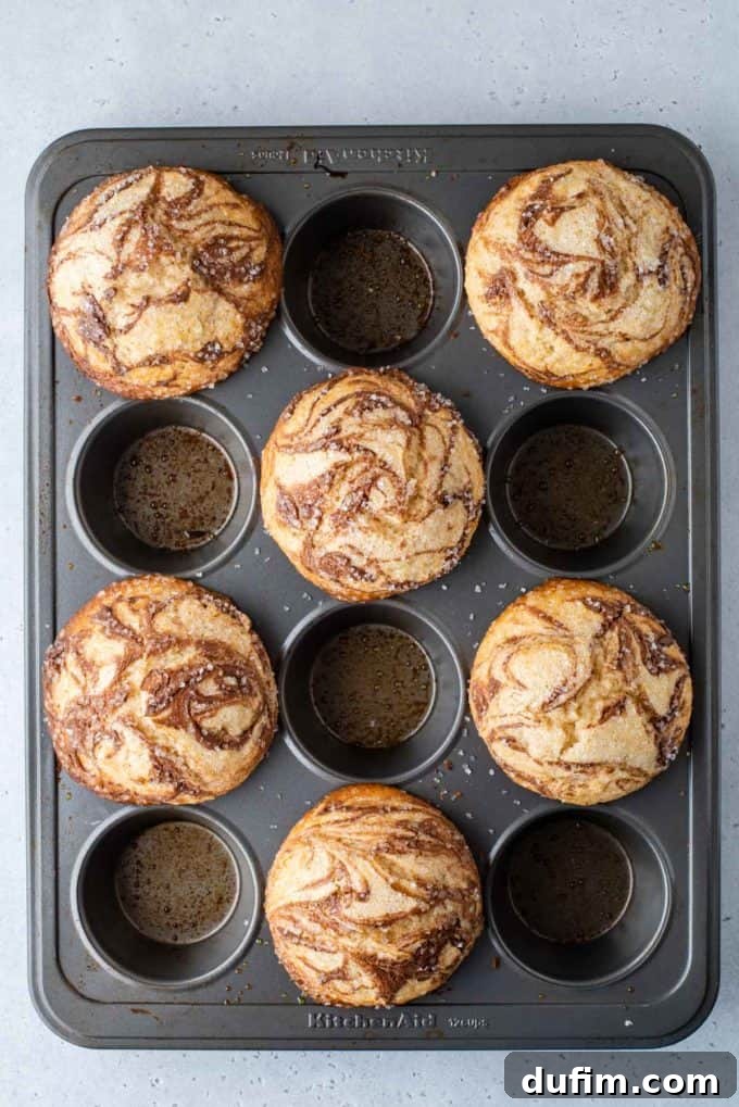 A muffin pan showcasing freshly baked Nutella swirl muffins, perfectly risen and golden, filling every other hole of the pan.