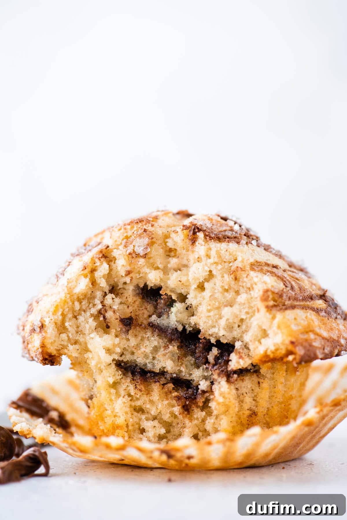 A Nutella swirl muffin, elevated on an open muffin liner, with a bite playfully missing, revealing the captivating Nutella layers within. It sits on a pristine white background.