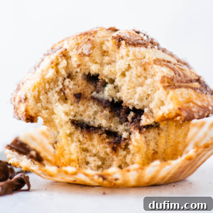 A Nutella swirl muffin on a white surface with a white background, with the muffin liner pulled away from the muffin exposing the layers of Nutella inside.