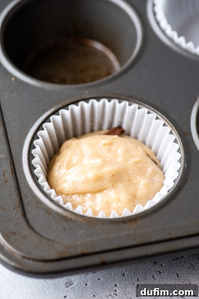 A muffin pan featuring a white muffin liner in a corner spot, showcasing distinct layers of muffin batter and Nutella carefully placed inside the liner.