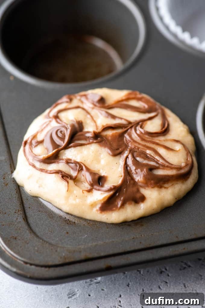 A muffin pan showcasing Nutella swirl muffin batter in one of the corner spots, ready for its final topping.