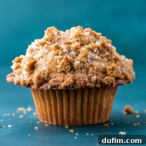 A maple pecan muffin on a dark teal surface with bits of the crumb topping surrounding it, showcasing its perfect texture and appealing appearance.