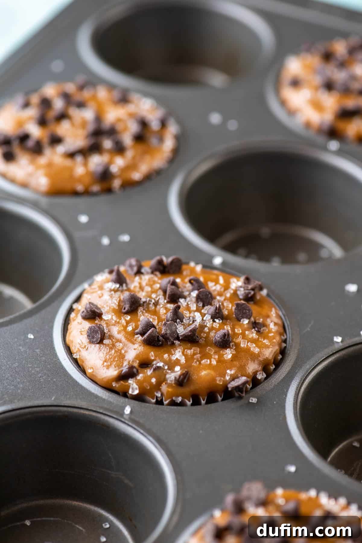 Café Mocha Chip Muffins 6 Cappuccino chip muffin batter filling every other hole of a muffin pan, topped with mini chocolate chips and sprinkled with sanding sugar.