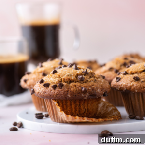 A plate of cappuccino chip muffins with chocolate chips and two cups of cappuccino in the background.
