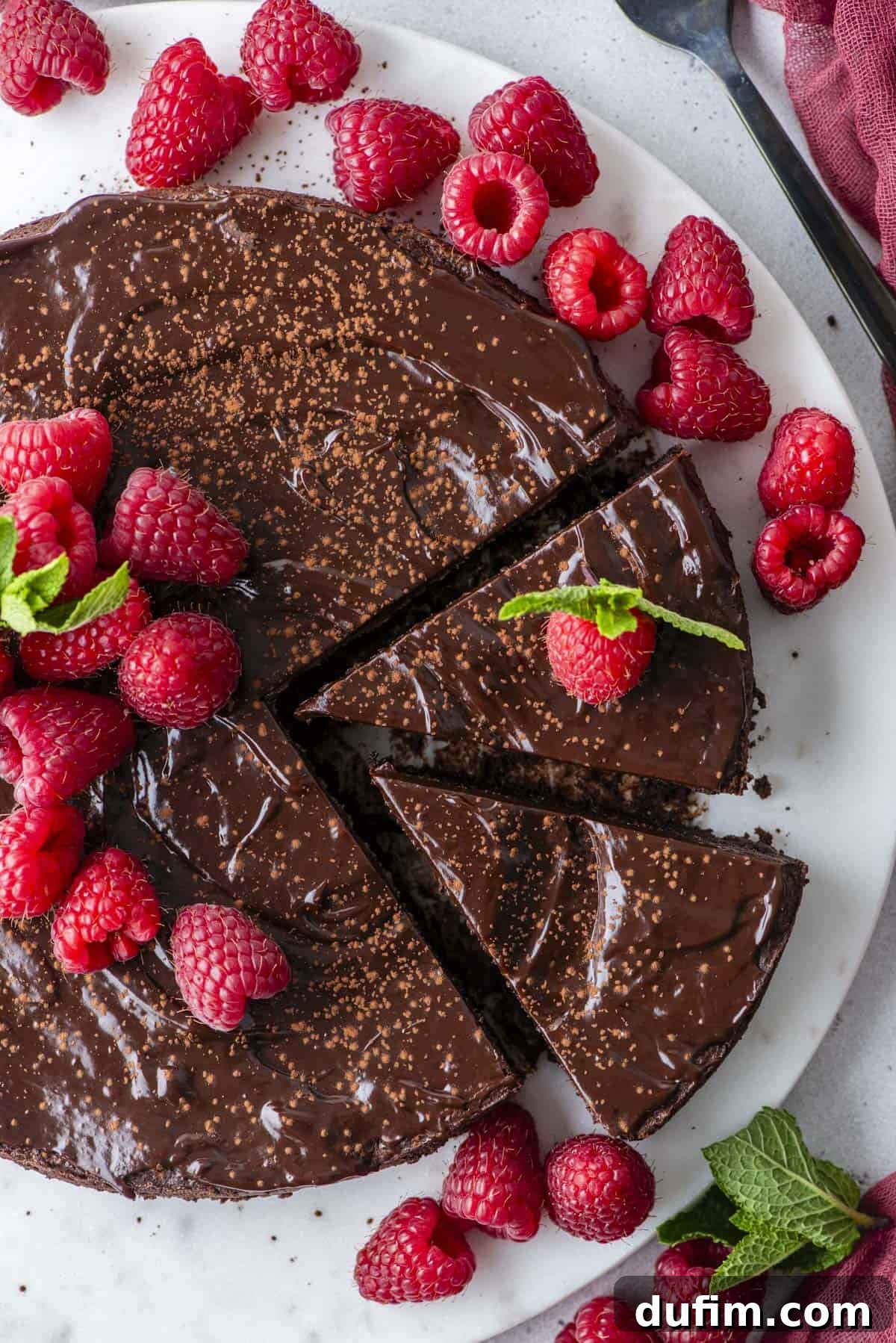 Decadent Flourless Chocolate Cake 2 overhead view of a flourless chocolate cake with two slices cut, sitting on a white plate and topped with fresh raspberries and mint leaves