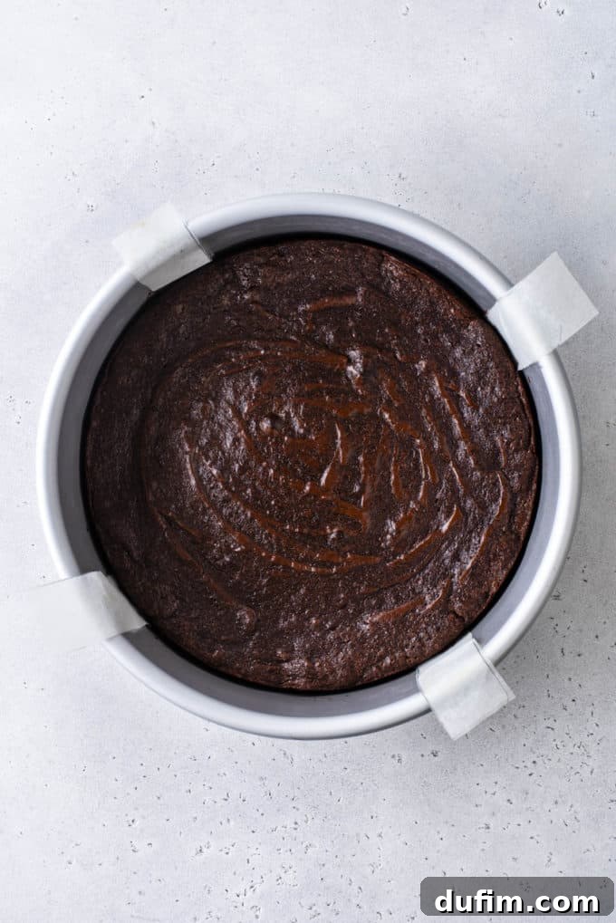 Decadent Flourless Chocolate Cake 15 freshly baked flourless chocolate cake in a round cake pan with four parchment paper handles sticking out the sides